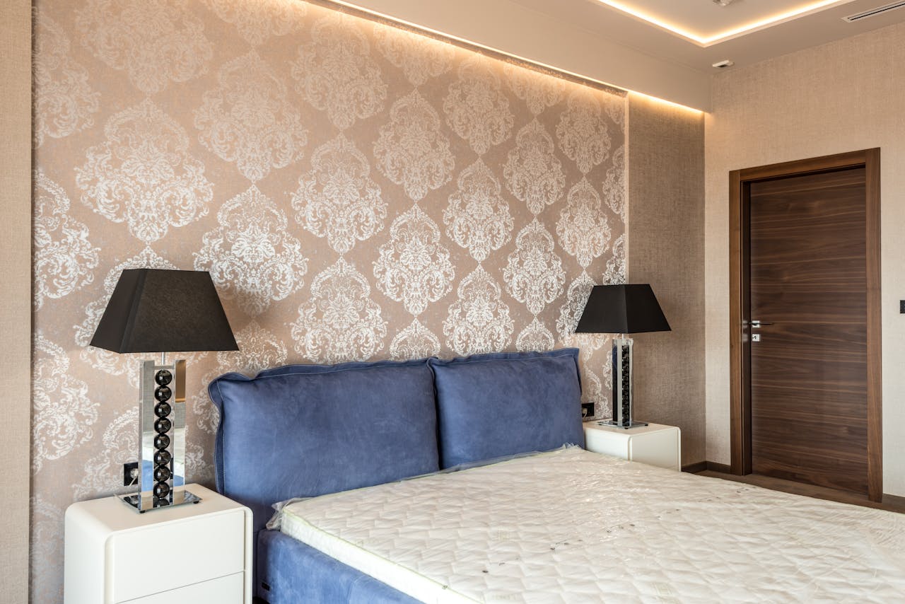 Modern bedroom featuring elegant wallpaper, blue headboard, and stylish black lamps for a contemporary look.